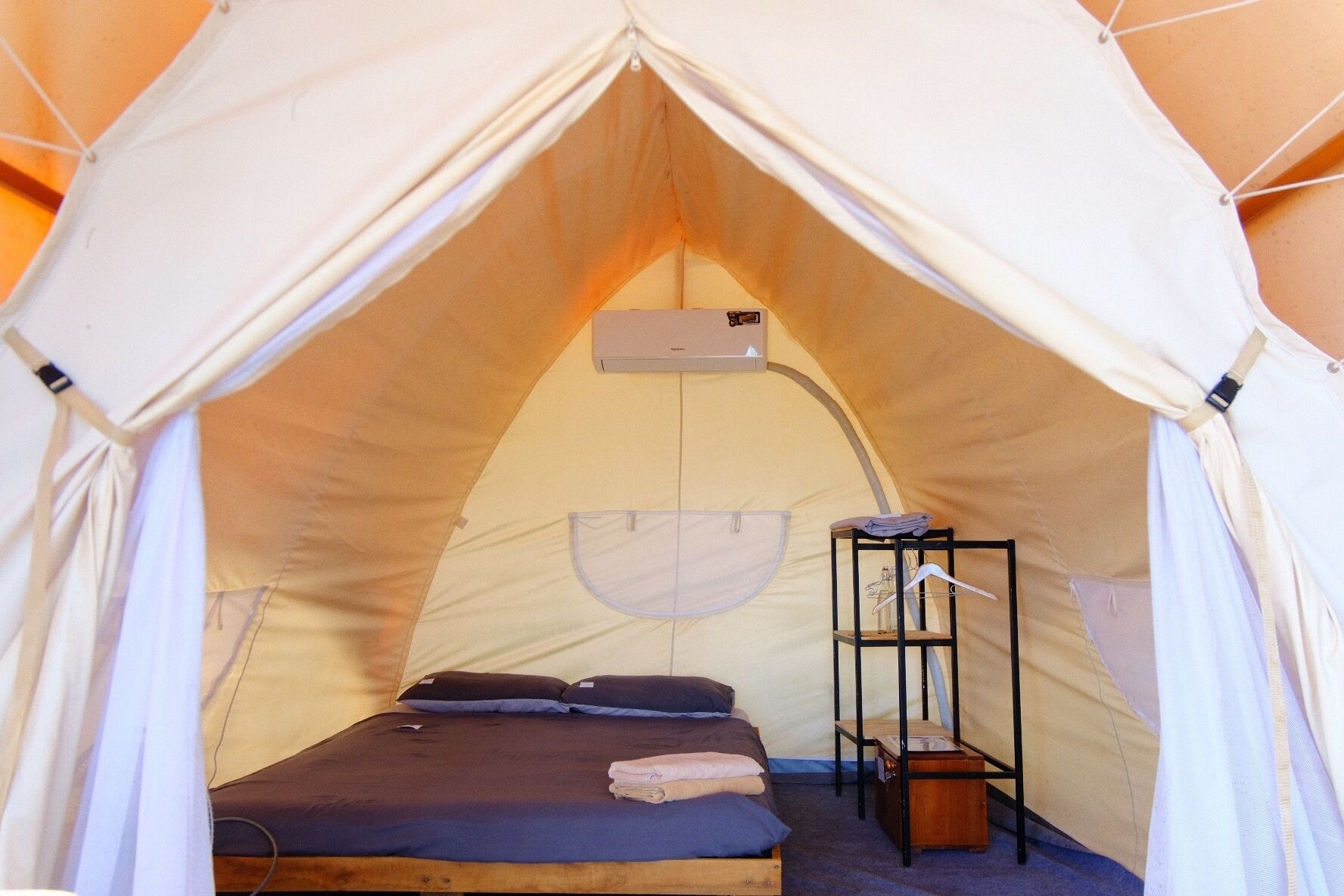 Une tente équipée d’un lit, d’une étagère et d’un appareil de climatisation.