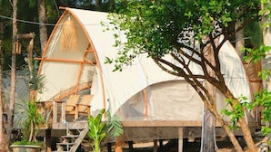A rustic tent with a ladder and a chair, surrounded by trees and potted plants.