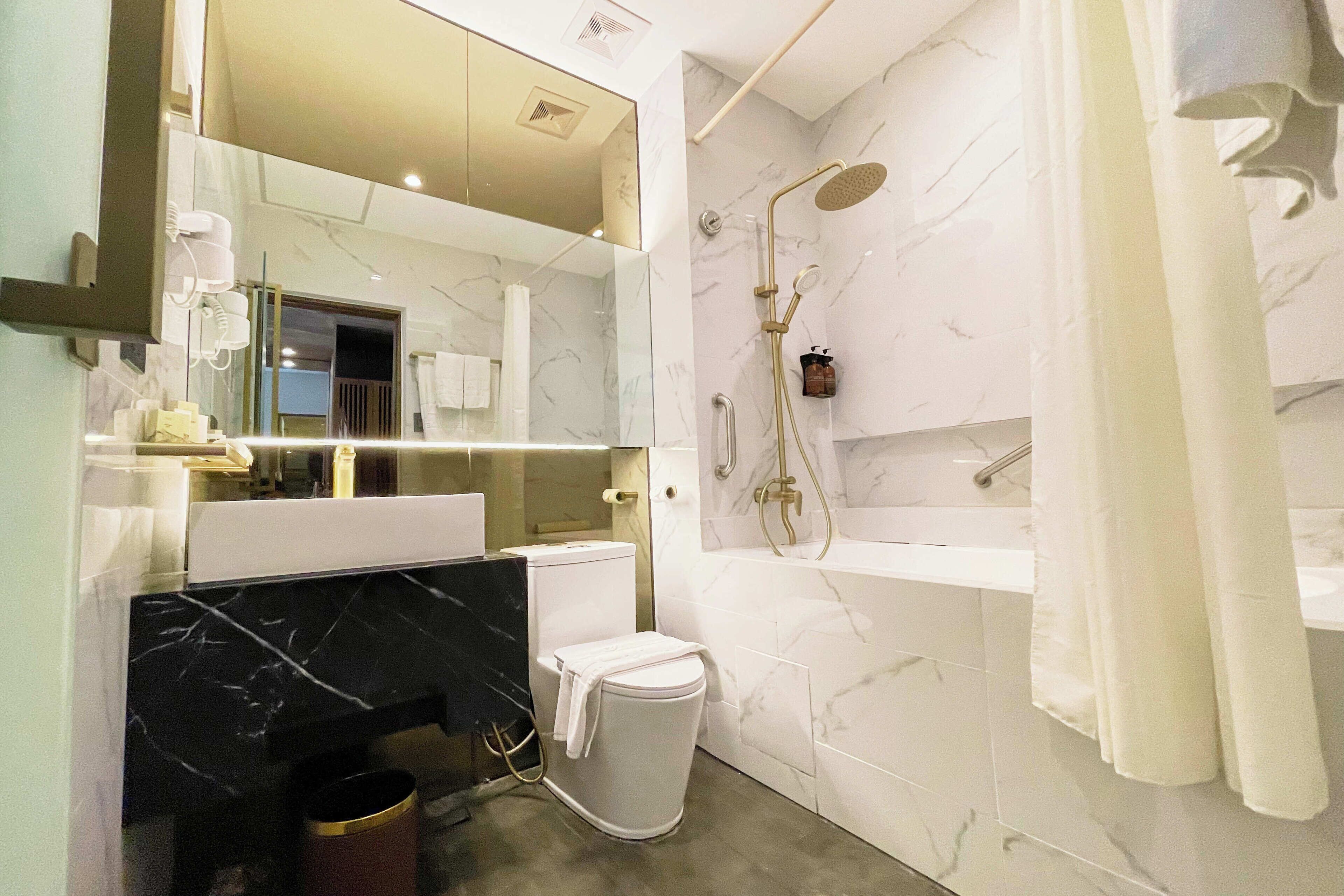 A modern bathroom with a marble vanity, a toilet, a shower with a handheld showerhead, and a towel rack.