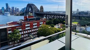 Un edificio moderno con fachada de vidrio que ofrece vistas a un paisaje urbano, incluyendo un puente distintivo y rascacielos.