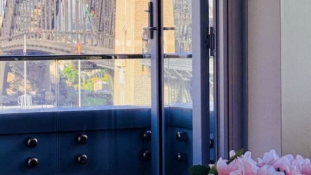 Una habitación con vistas a un puente grande y edificios, una ventana con vistas, y un jarrón con flores sobre una mesa.