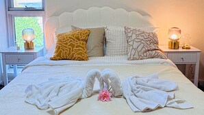 Una cama bien hecha con una colcha blanca, dos almohadas y una decoración de toallas con forma de cisne.