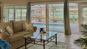 A spacious living room with a sofa, coffee table, and large windows overlooking a pool area. - Luxury Oceanfront 3BR with Pool, Dock & Boat Lift (Cortez)