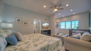 A bedroom with a bed, a sofa, a TV, and a ceiling fan. - 2 Units | Beach Boardwalk, Pool, Pickleball + Tennis | Island Retreat Complex (Port Aransas)