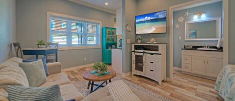 Una sala de estar con un sofá, una mesa de centro y un televisor. Cuenta con una zona de cocina con armarios y una encimera.