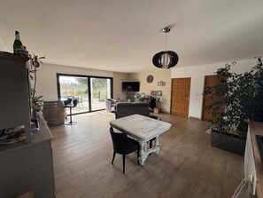 Un vaste espace de vie comprenant une table à manger, un canapé et un téléviseur fixé au mur. Une porte-fenêtre coulissante donne accès à un patio extérieur.