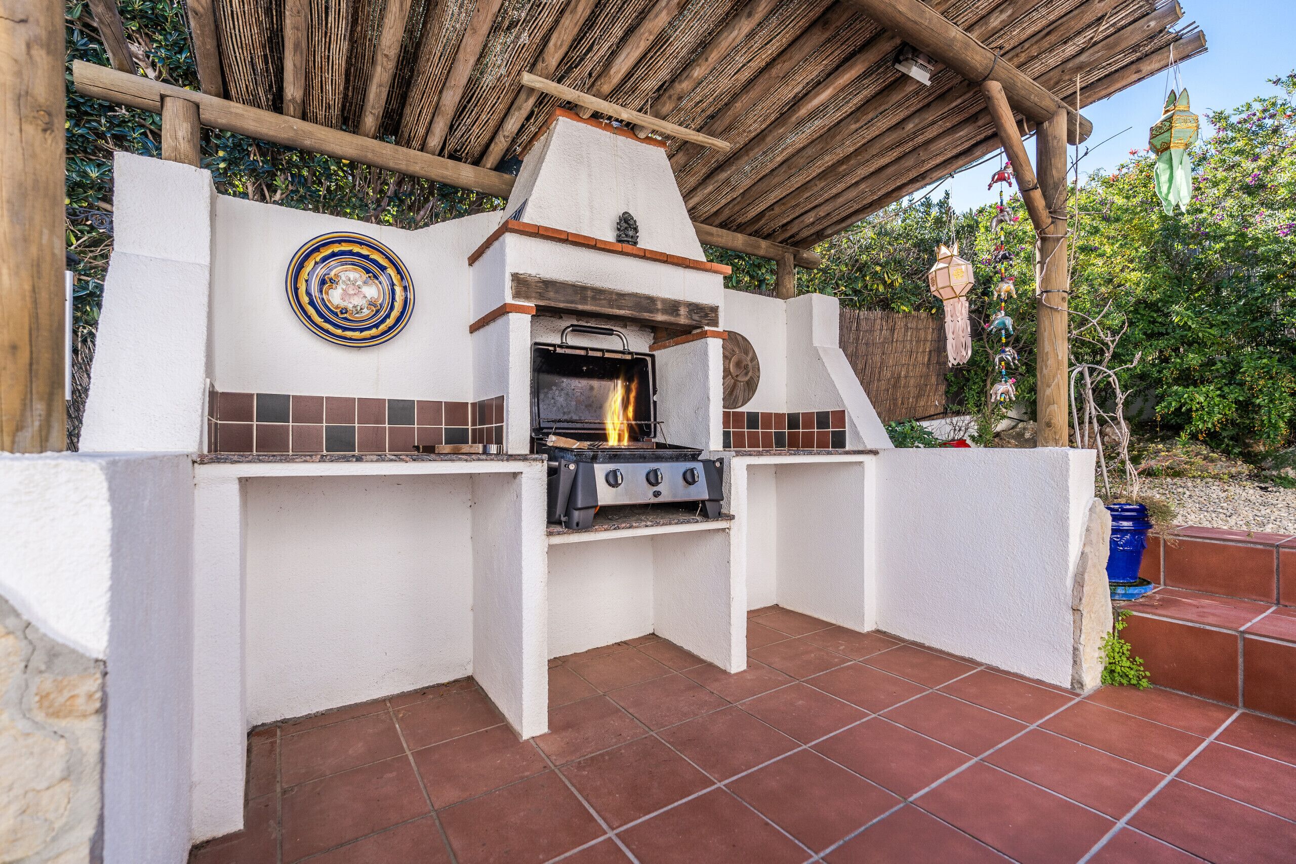 An outdoor kitchen with a grill, a decorative plate, and a hanging lantern.