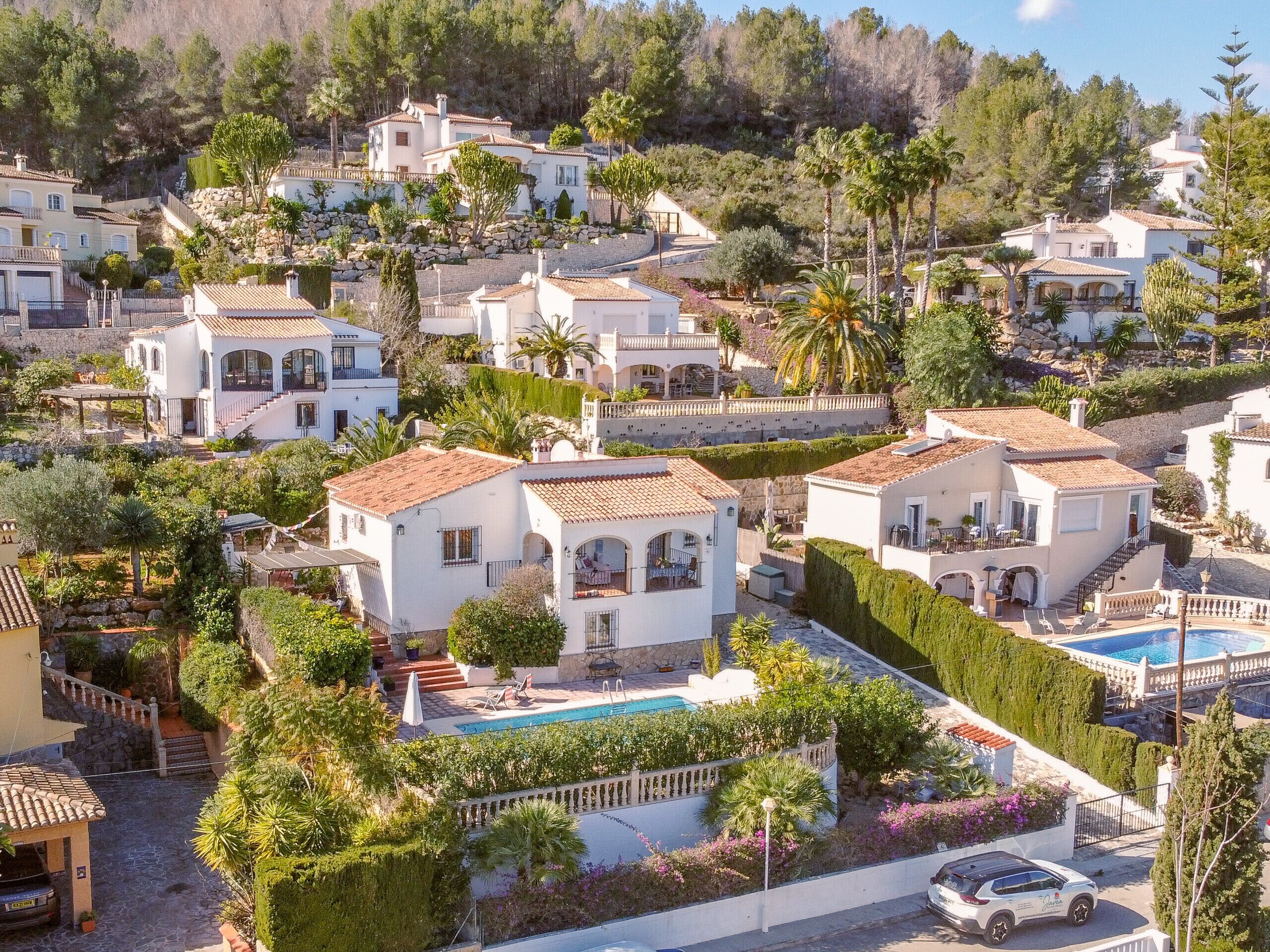 Zona residencial con varias casas blancas, una piscina y un coche estacionado en la calle.