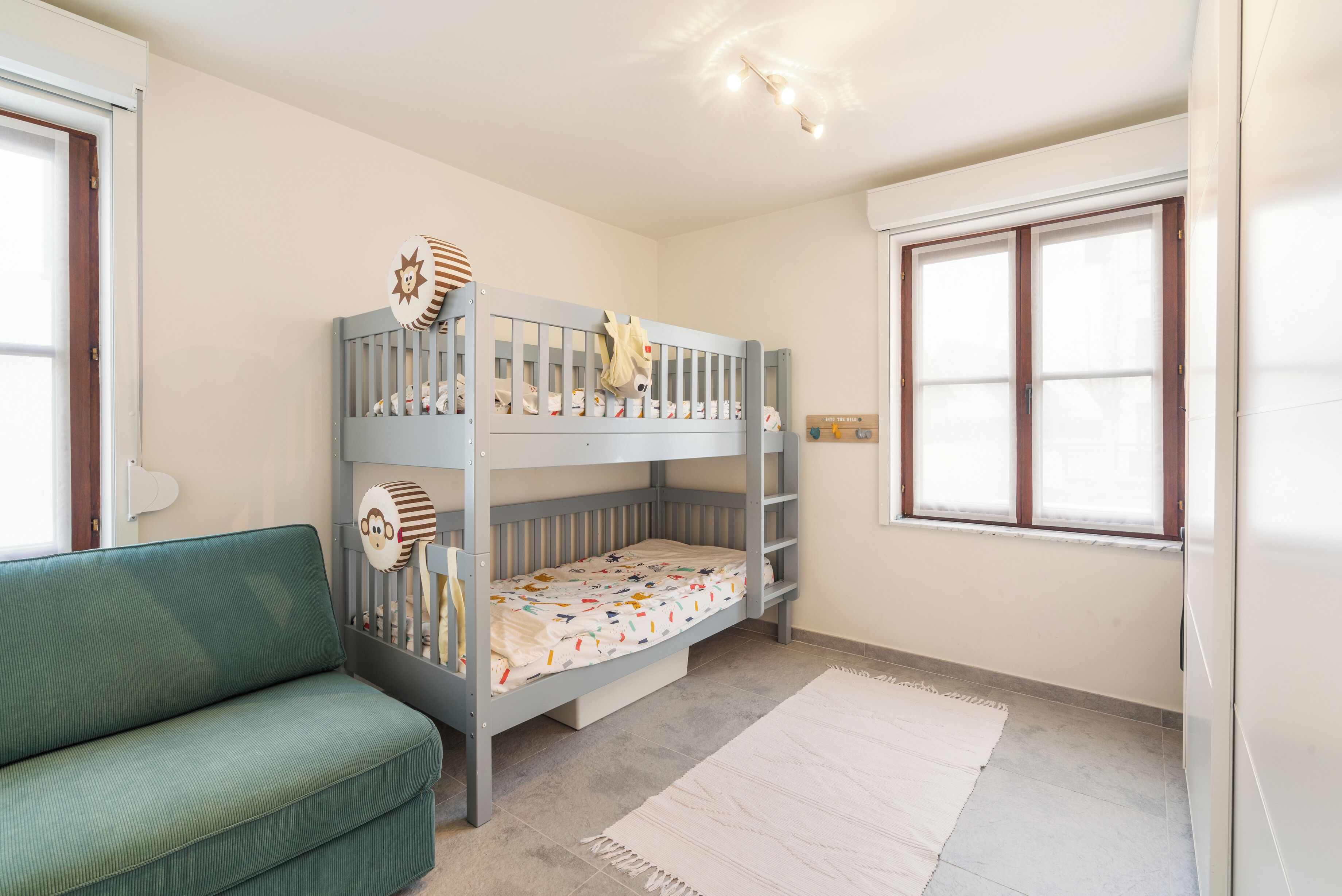 Habitación infantil con una cama litera, un sofá verde, una ventana y una alfombra blanca.