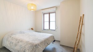 Ein Schlafzimmer mit Bett, Fenster, einer Holzleiter und einer Pendelleuchte.