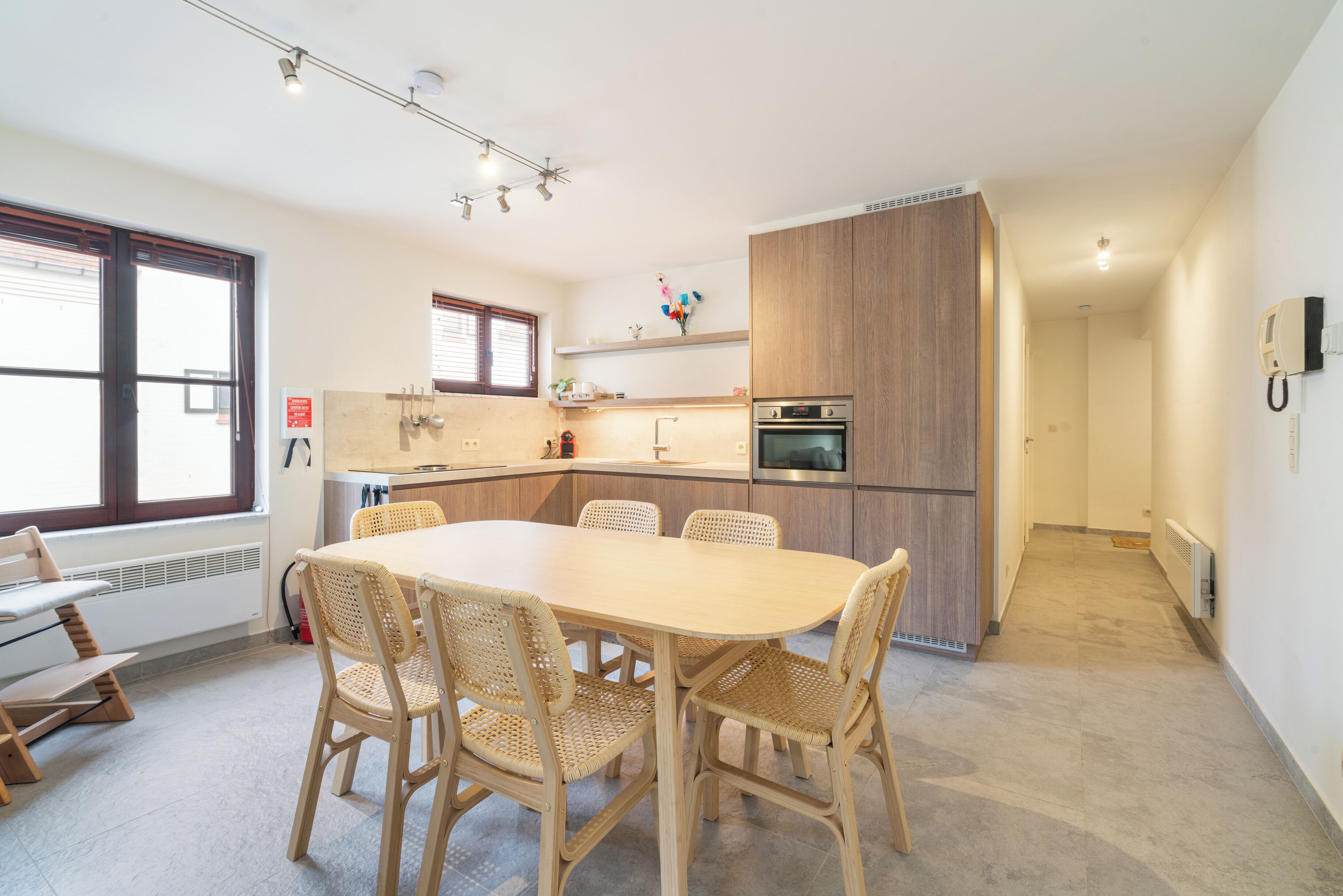 Una cocina moderna con una isla central, horno empotrado y un comedor con mesa redonda y sillas de mimbre.