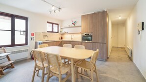 Eine moderne Küche mit einer zentralen Kochinsel, einem eingebauten Backofen und einem Essbereich mit rundem Tisch und Korbstühlen.