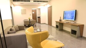 A modern living room with a sofa, a yellow armchair, a glass coffee table, a TV, and a kitchen area in the background. - The Mark Hotel  (Manama)