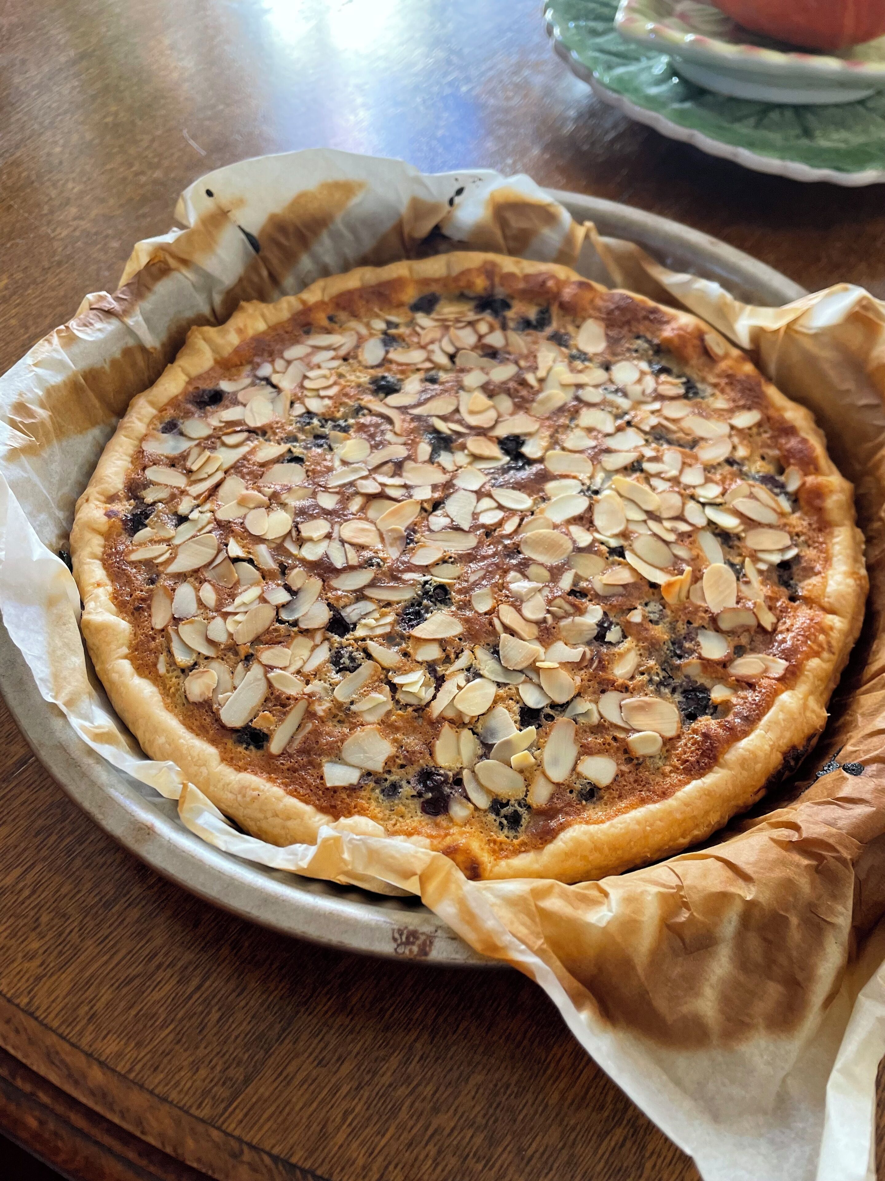Une tarte ronde, recouverte d’amandes effilées, posée sur un plateau en métal recouvert de papier sulfurisé.