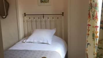 Una cama individual con cabecera y piecera blancos, una pared lisa con un pequeño cuadro enmarcado, y una alfombra a rayas en el suelo.