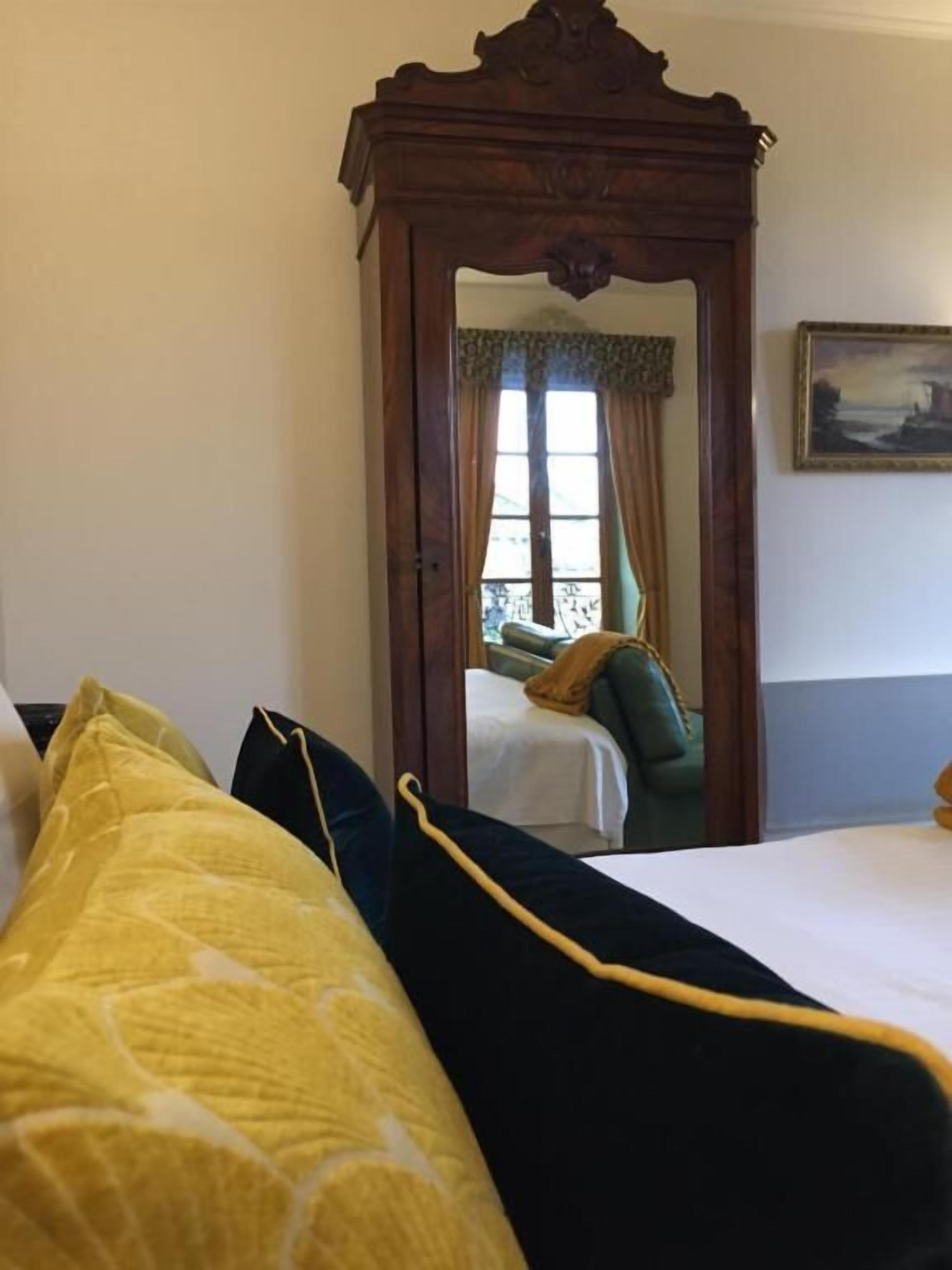 Ein Hotelzimmer mit einem großen Spiegel, einem Bett mit gelb-schwarzer Bettwäsche und einem Gemälde an der Wand.