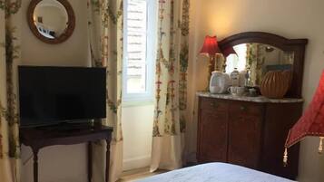 A bedroom with a bed, a TV on a stand, a dresser, a mirror, and curtains.