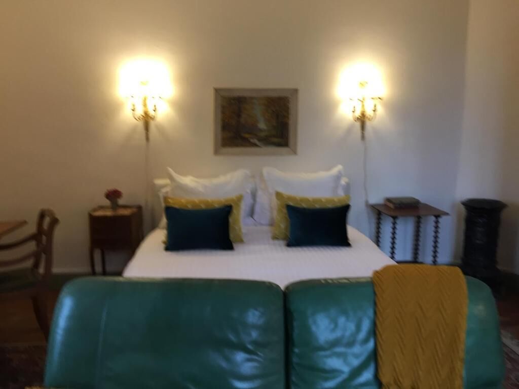 Habitación de hotel con una cama grande, dos lámparas de pared, un cuadro en la pared y una mesita con una lámpara.