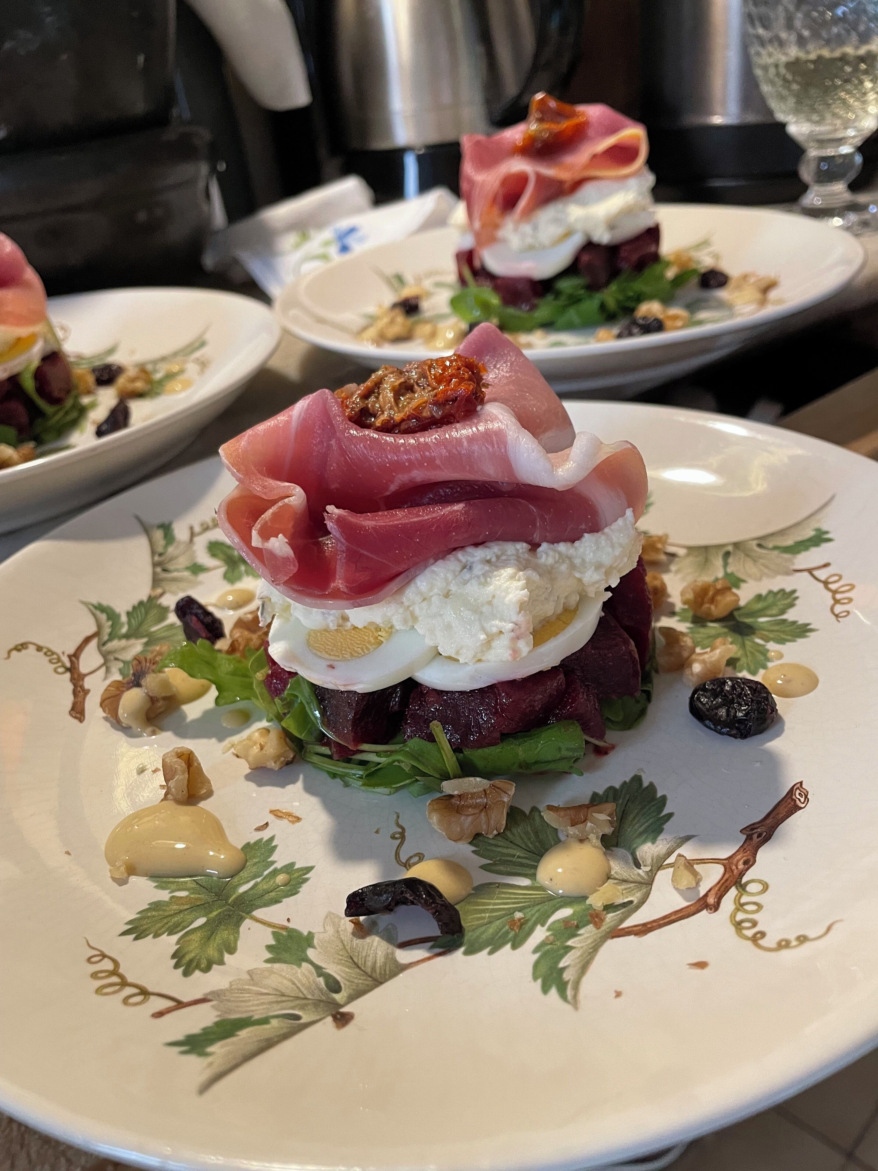 A plated dish with a layered arrangement of ingredients, including a red meat base, a white creamy layer, and a topping of thinly sliced red meat.