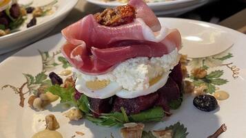 Un plat composé de différentes couches d’ingrédients, notamment une base de viande rouge, une couche crémeuse blanche et une garniture de fines tranches de viande rouge.