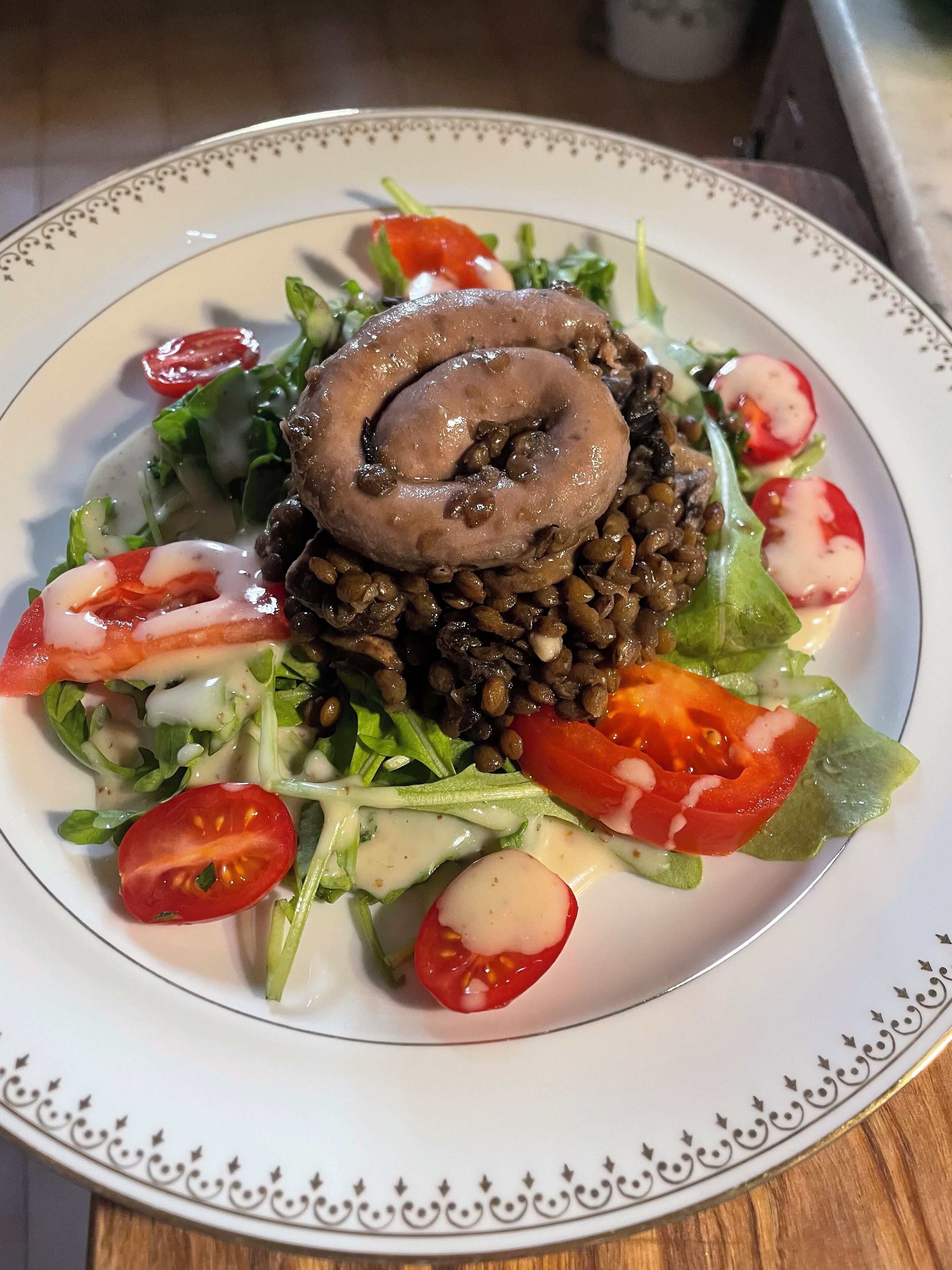 Un plato de comida con carne enrollada, lentejas y ensalada.
