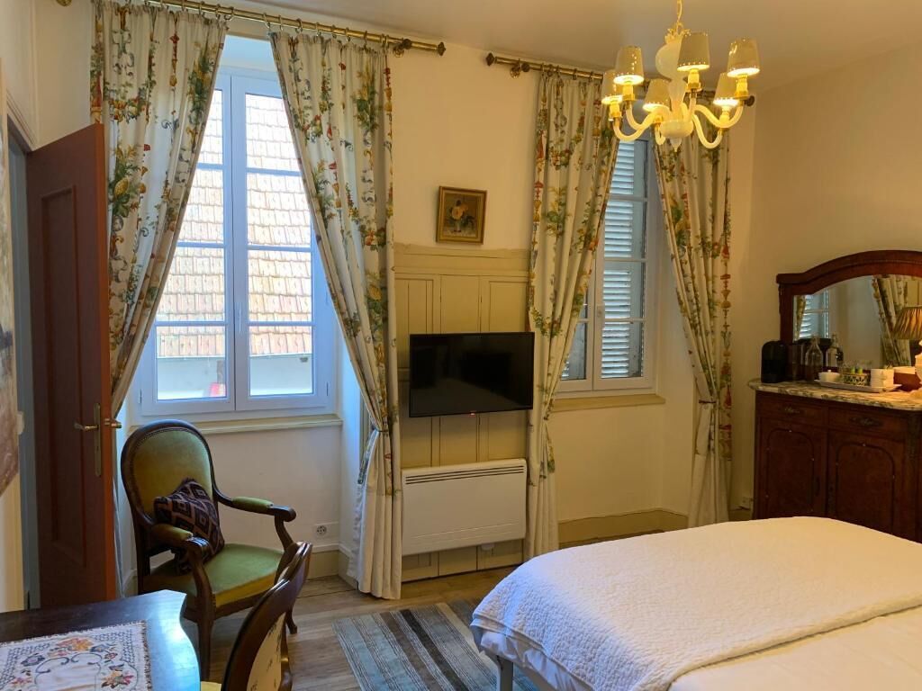 Un dormitorio con cama, una silla, televisor, cómoda y candelabro.