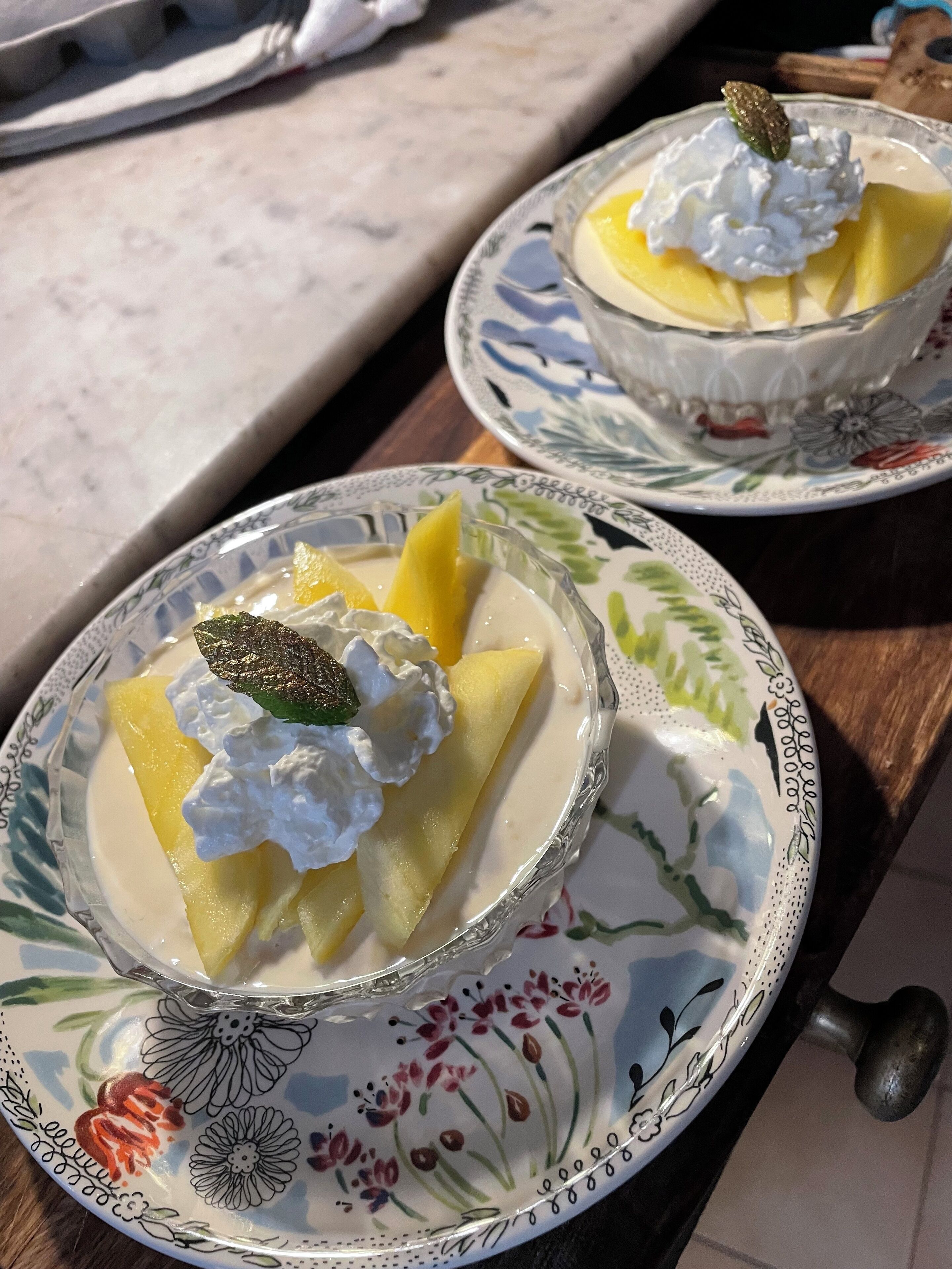 Two bowls of dessert with fruit and whipped cream on decorative plates.
