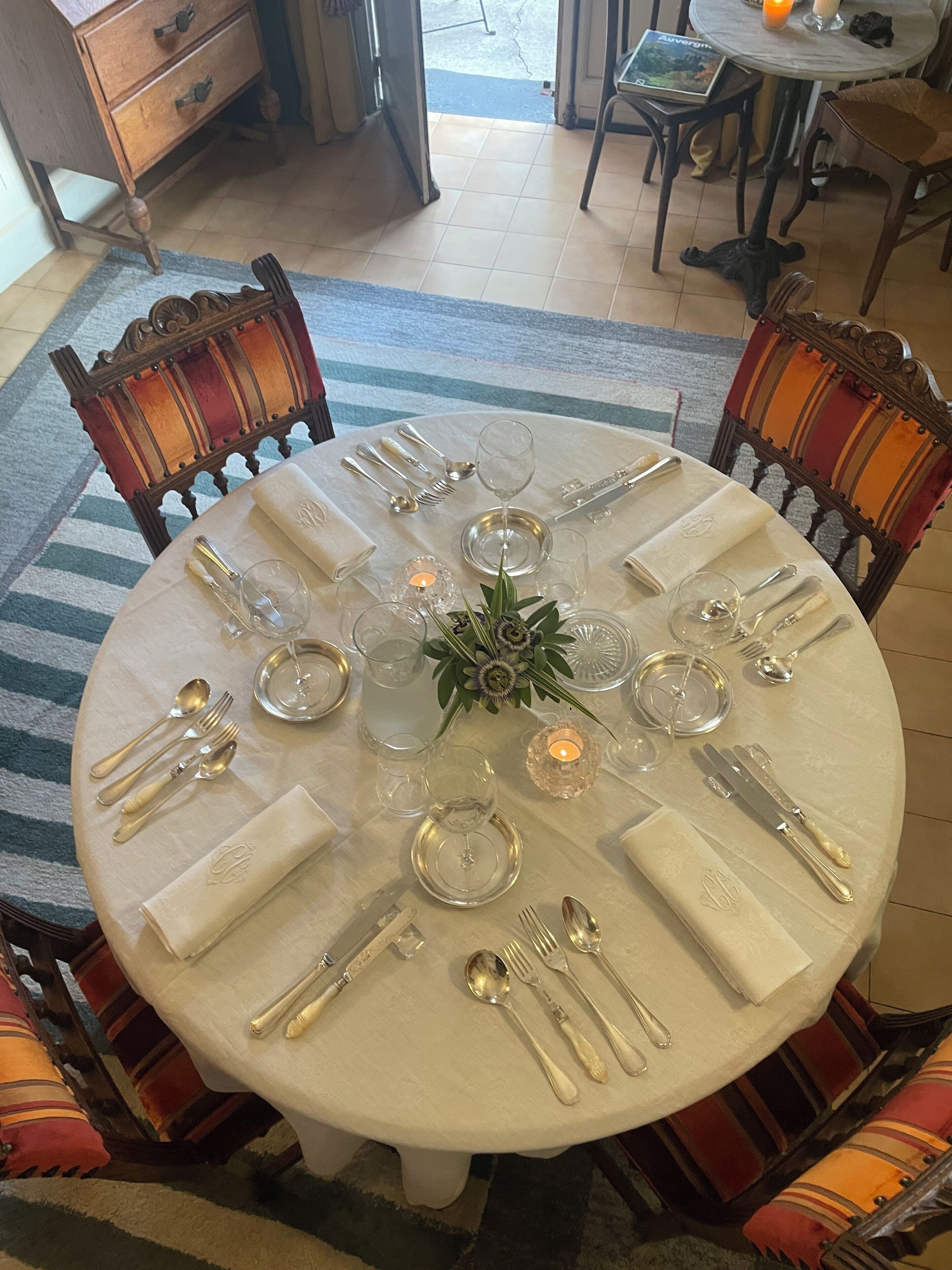 A round dining table set for six with a white tablecloth, silverware, and glassware.