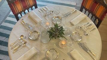 A round dining table set for six with a white tablecloth, silverware, and glassware.