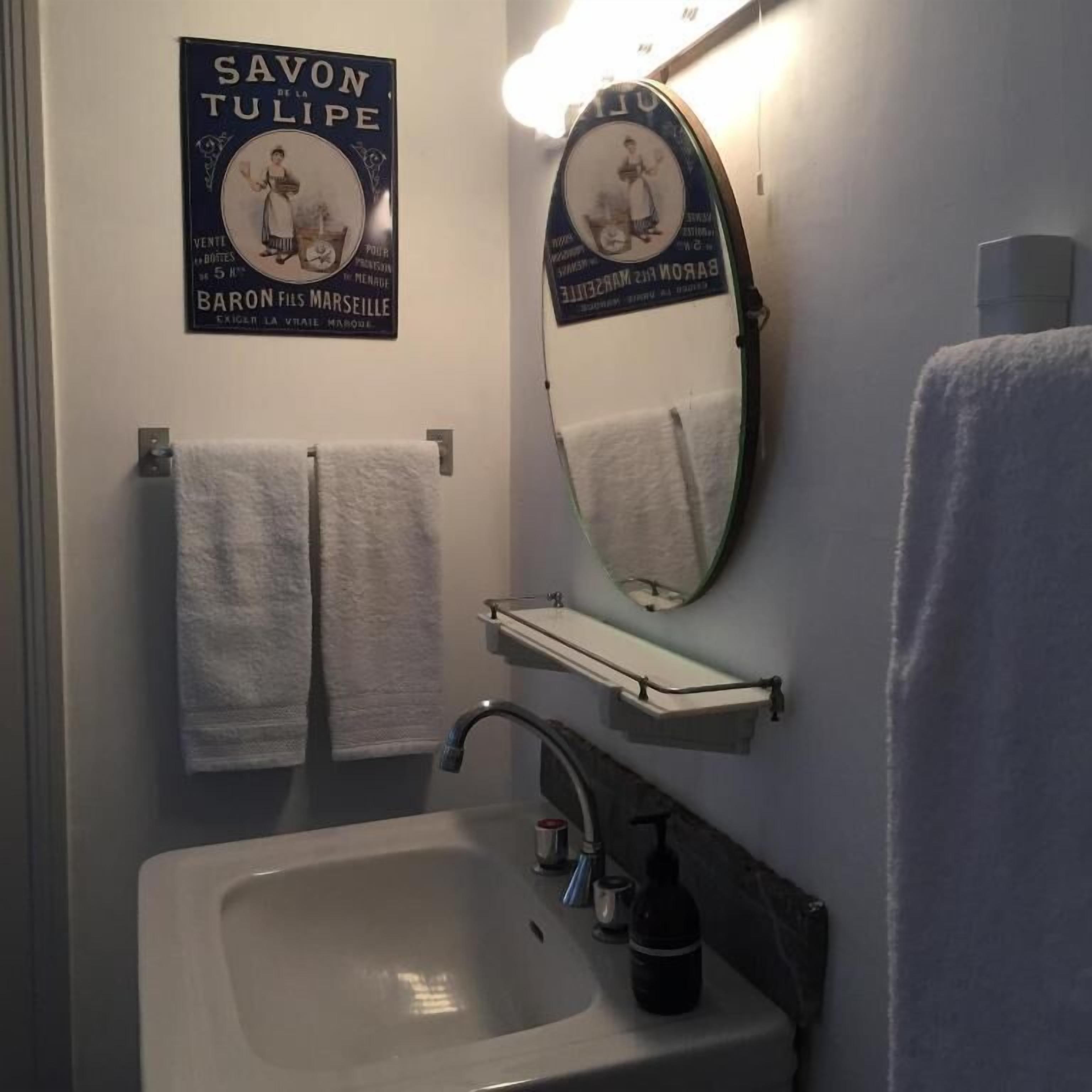 A bathroom with a white sink, a mirror, and two white towels hanging on the wall.