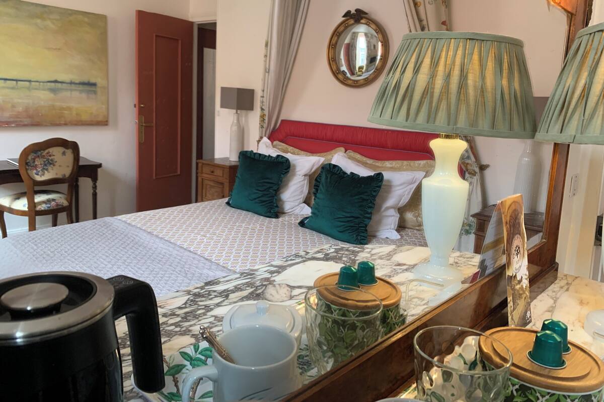 Un dormitorio ordenado con cama, lámparas de noche, un espejo y un escritorio con silla.
