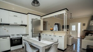 A modern kitchen with white cabinets, a granite countertop, and a dining area with a table and chairs. - Ionian View Village House (Zakynthos)
