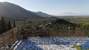 A terrace with a patterned floor, a wooden fence, and a view of a town and mountains. - Ionian View Village House (Zakynthos)