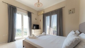 A bedroom with a bed, curtains, a TV, a dresser, and a balcony view. - Ionian View Village House (Zakynthos)