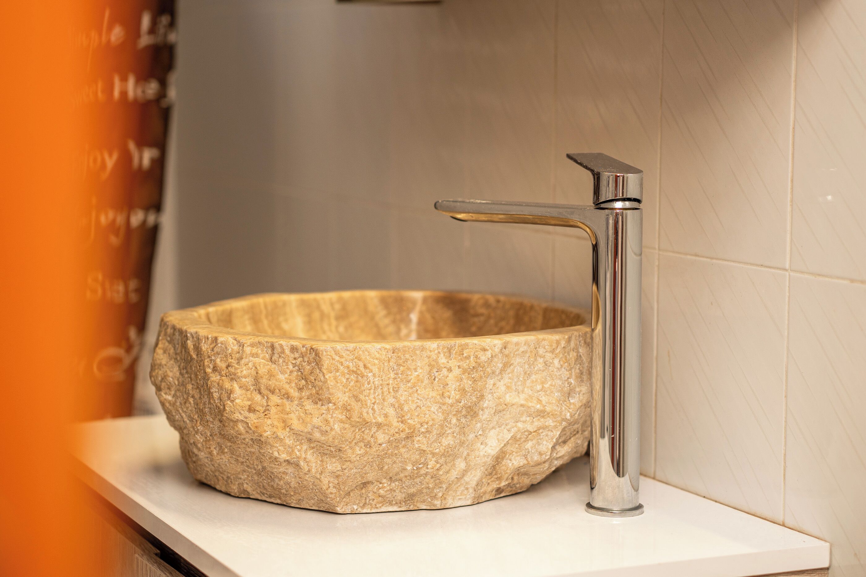 Ein Becken aus Stein mit einem modernen Wasserhahn auf einer weißen Arbeitsplatte.