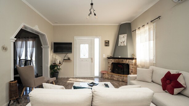A living room with a fireplace, a sofa, a television, and a door leading to another room. - Ionian View Village House (Zakynthos)