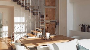 A modern interior with a wooden dining table, white chairs, a white sofa, and a staircase with wooden railings.