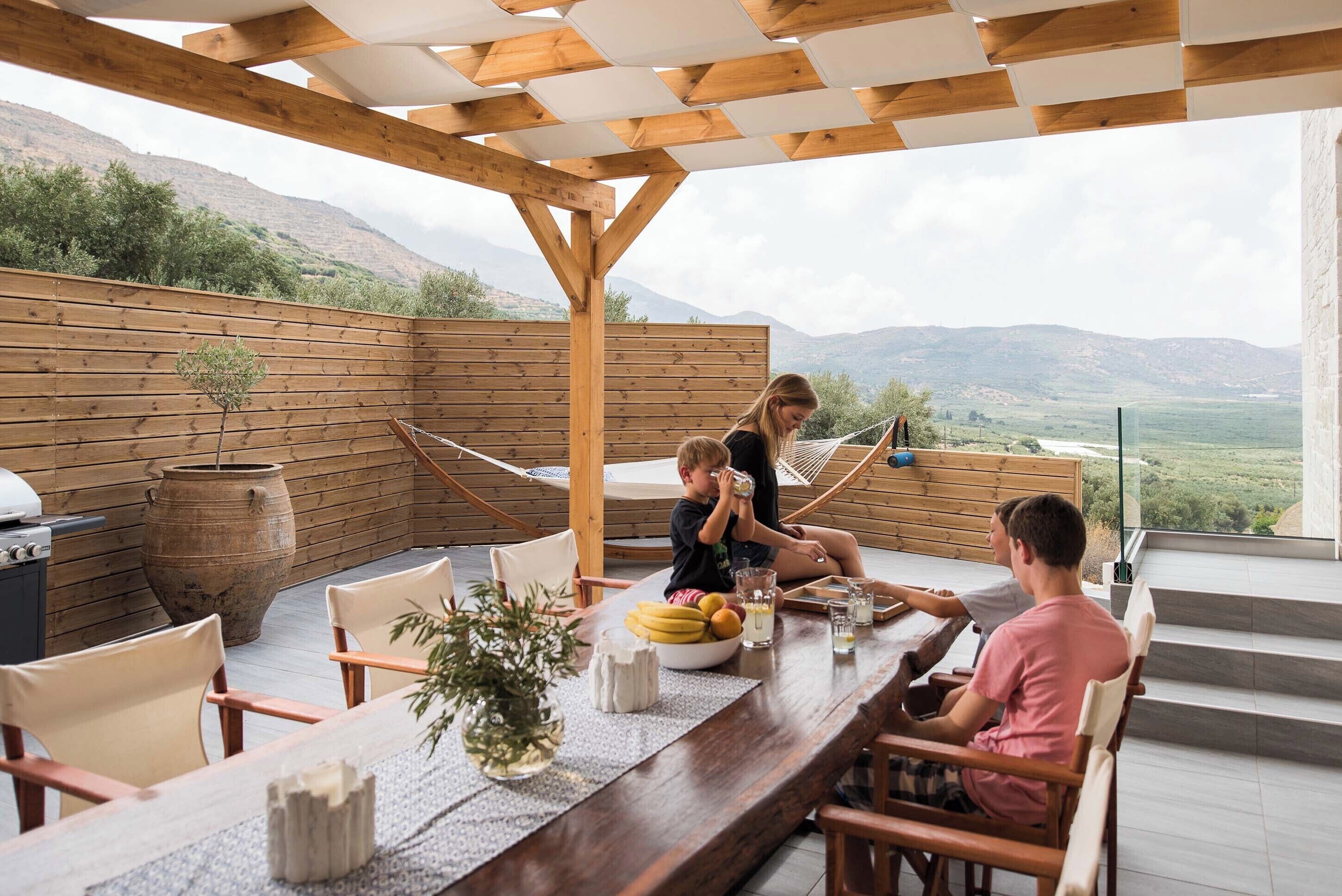 An outdoor dining area with a wooden pergola, a table set with chairs, and a scenic mountain view.