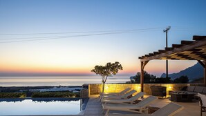 Ein Infinity-Pool mit Liegestühlen und einer Pergola mit Blick auf einen Sonnenuntergang.