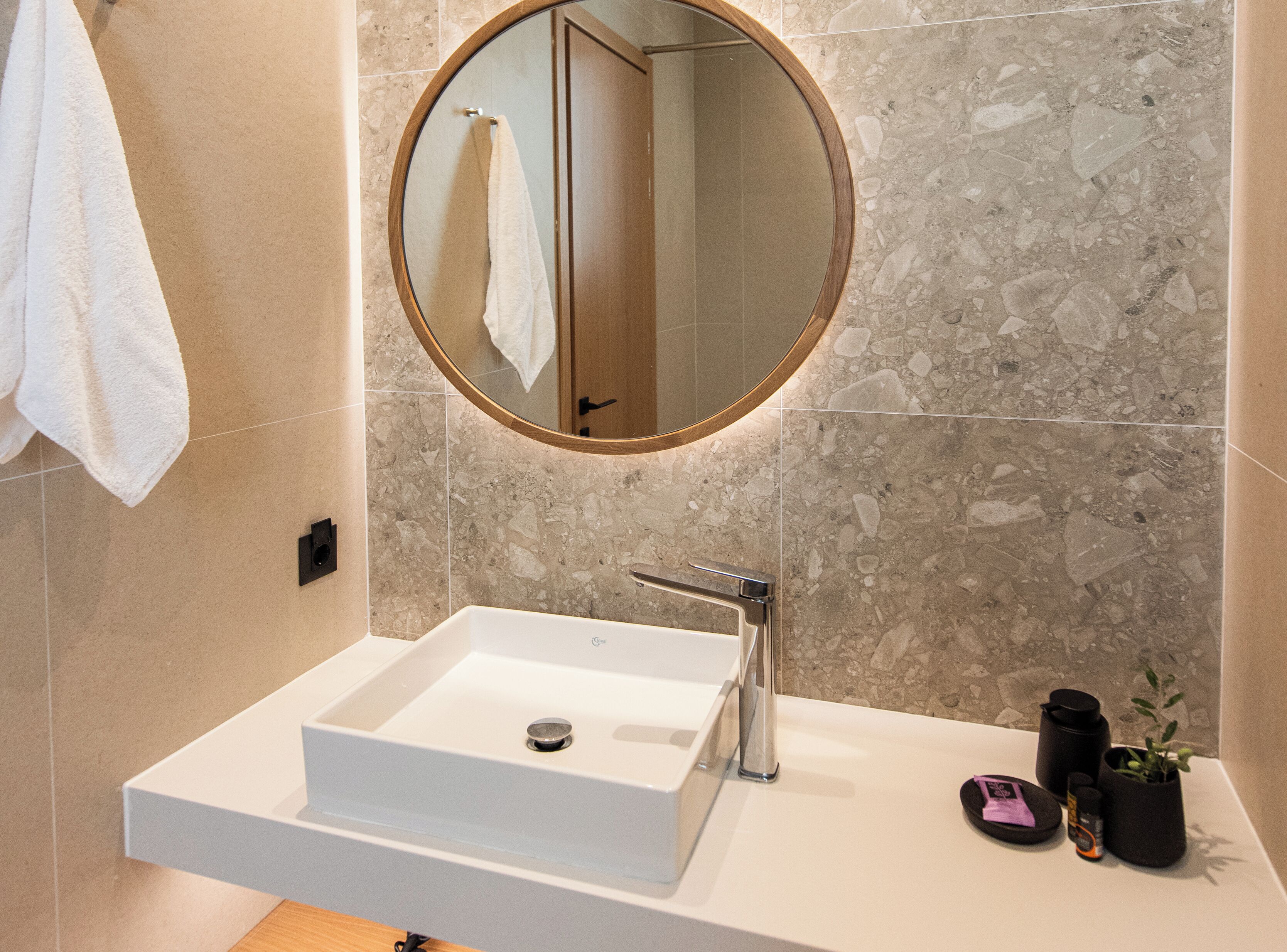 Une salle de bain avec un lavabo blanc, un miroir rond et une serviette accrochée au mur.