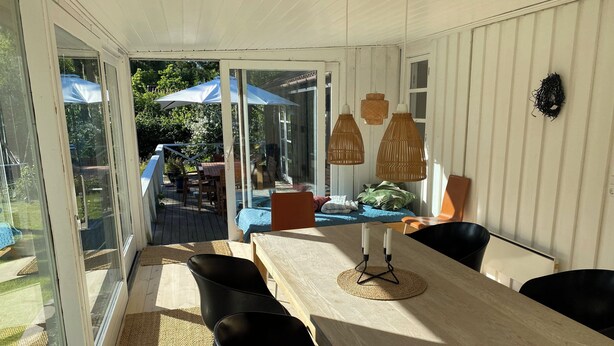 A sunlit room with a wooden table, black chairs, and a glass door leading to an outdoor area with a table and chairs. - Lovely holiday home near Vejby Strand (Vejby)