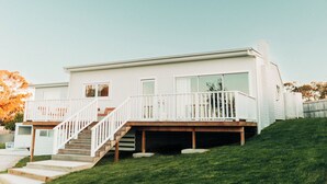 Una casa moderna de dos pisos con una terraza de madera y una escalera que lleva a un balcón.