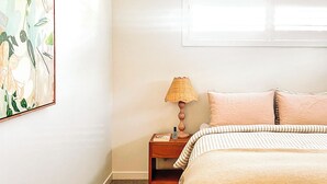 Un dormitorio con cama, mesita de noche, lámpara y un cuadro en la pared.