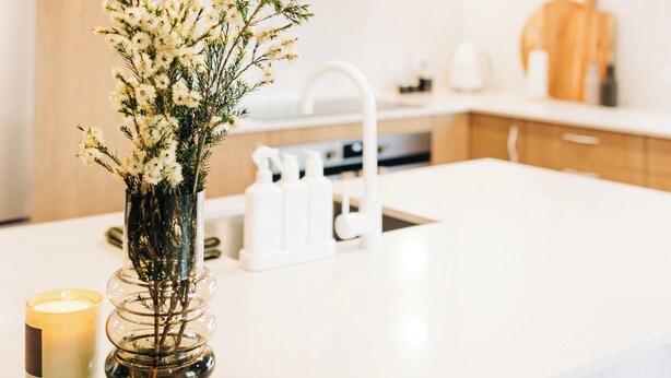 Una cocina moderna con armarios blancos, encimera blanca y un florero con flores.