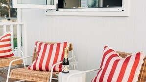 Un espacio de estar al aire libre cubierto con sillas de mimbre y cojines a rayas, una botella de champán y una mesa blanca.