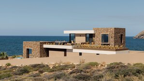 A modern coastal building with a flat roof, stone walls, and large windows. - Ormus Villa - An Earthy Beachfront Sanctuary by etouri (Rethymno)