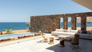 A modern outdoor lounge area with a stone wall, a pool, and a view of the sea. - Ormus Villa - An Earthy Beachfront Sanctuary by etouri (Rethymno)