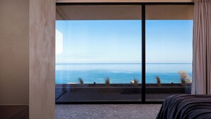 A bedroom with a large sliding glass door leading to a balcony with a view of the sea. - Ormus Villa - An Earthy Beachfront Sanctuary by etouri (Rethymno)