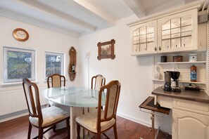 A dining area with a glass table, wooden chairs, a clock, and white cabinetry.
