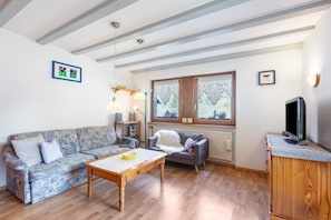Un salon comprenant un canapé, une table basse, un téléviseur et une fenêtre donnant sur un paysage verdoyant.